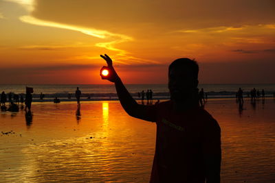 Optical illusion of man holding sun at beach during sunset