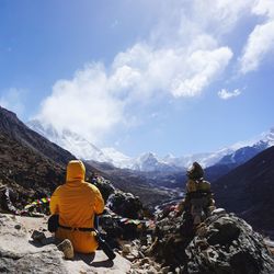 Rear view of woman wearing yellow jacket sitting on mountain against sky during winter