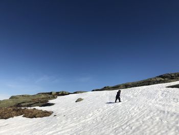 Girl walking up a snowcapped mountain against clear blue sky