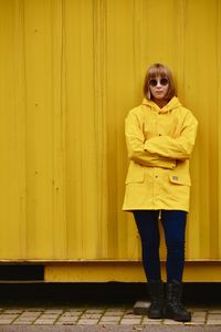 Portrait of young woman standing against yellow wall