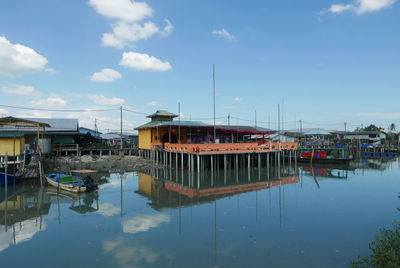 Sailboats moored at harbor against sky and buildings