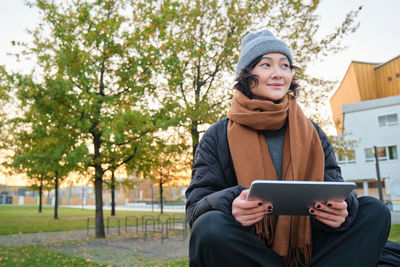 Portrait of young woman using mobile phone while sitting on field