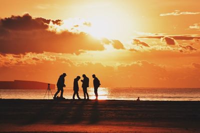 Silhouette people on beach against sky during sunset