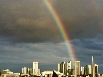 Rainbow over city against cloudy sky