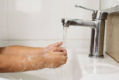 Cropped image of child washing hands in sink