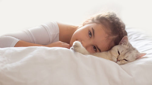 Wide banner. a beautiful little girl in white clothes, lies on a clean, white bed with a white cat.