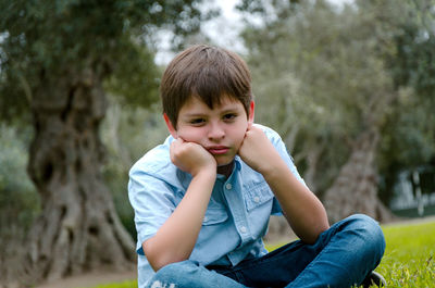 Portrait of sad boy sitting at park
