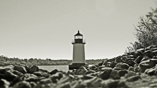 Lighthouse by sea against clear sky