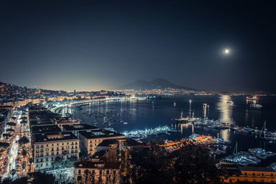 High angle view of illuminated city by sea against sky