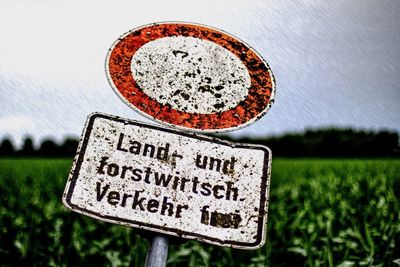 Close-up of road sign on field against sky