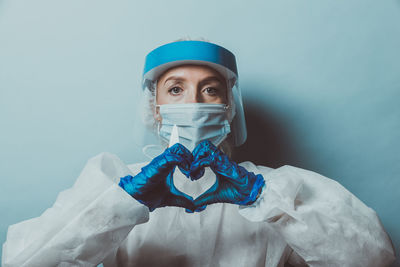 Portrait of doctor wearing mask making heart shape against wall