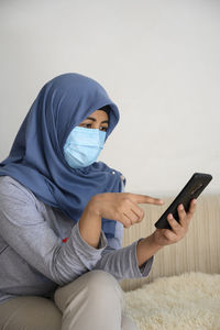 A hijab woman is wearing masker while looking at her smartphone in covid 19 pandemic situation