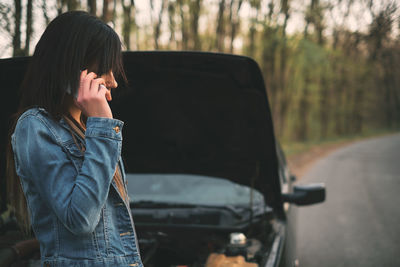 Side view of woman using phone by breakdown car on road