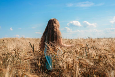 A long-haired fair-haired girl walks in a golden field of rye. view from the back. the freedom 