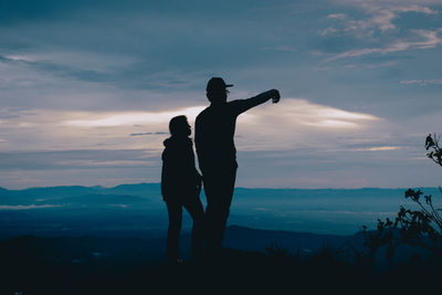 Silhouette man gesturing while standing by woman on mountain against sky during sunset