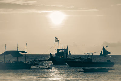 Sailboats moored on sea against sky during sunset