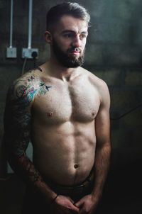 Thoughtful shirtless man standing against wall