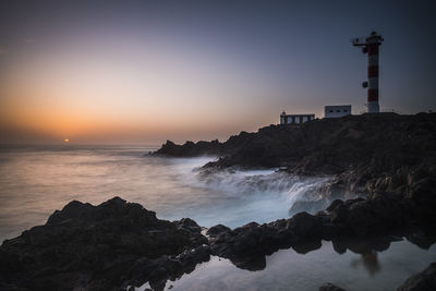 Lighthouse by sea against sky during sunset