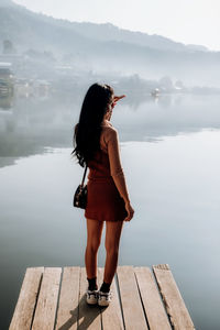 Woman standing on pier over lake against mountain