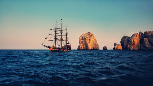 Sailing ship in sea against clear sky during sunset