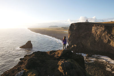 Man standing on cliff by sea against sky