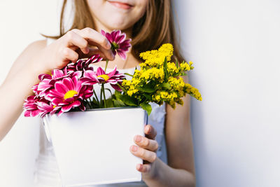 Midsection of girl holding flowers against wall