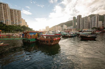 Boats moored in river by buildings against sky