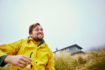 Low angle view of smiling man holding smoking pipe on field against clear sky