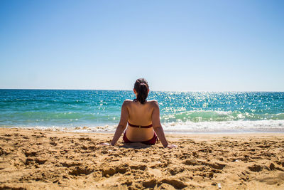 Rear view of shirtless man on beach against clear sky