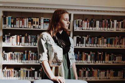 Young woman standing against bookshelf in library