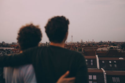 Rear view of friends standing with arms around while looking at city during party