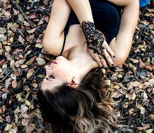 High angle view of beautiful young woman lying on field with dried leaves