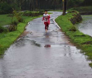 Full length of boy walking on wet road during rainy season