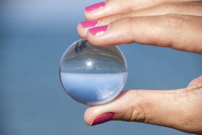 Cropped hand of woman holding crystal ball against sea
