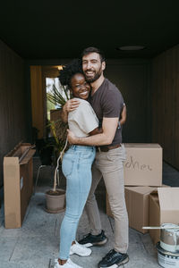 Side view portrait of happy multiracial couple embracing each other while standing at building entrance