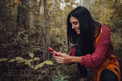 Young woman photographing plant with smart phone in forest