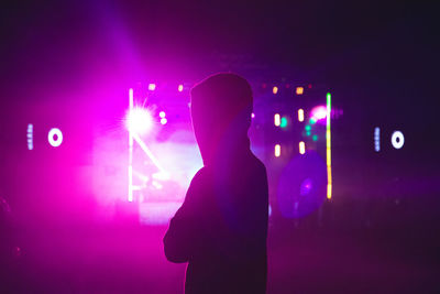 Silhouette man standing against illuminated light at night