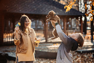 Happy family mother and teen boy son having fun with cocker spaniel puppy in autumn park