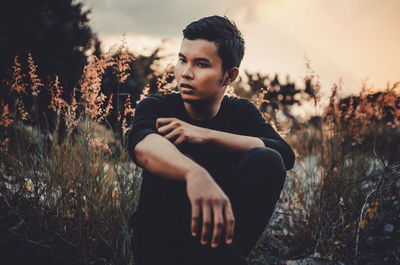 Portrait of young man looking away while sitting on land