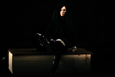 Full length portrait of woman sitting against black background