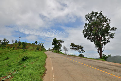 Empty road amidst trees against sky