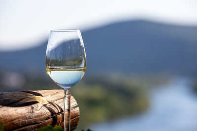 Filled wine glass next to wooden beam and defocused moselle valley in background