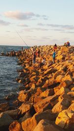 People fishing at sea shore against sky