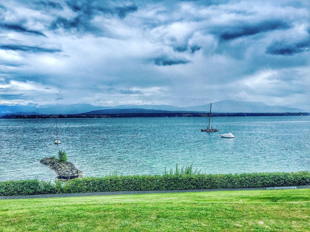 nautical vessel, transportation, grass, mode of transport, cloud - sky, water, boat, sky, tranquility, tranquil scene, blue, cloudy, scenics, sailboat, nature, day, mountain, cloud, non-urban scene, beauty in nature, outdoors, cloudscape, calm, journey, mountain range, tourism, no people, sea, shore, dramatic sky