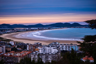 High angle view of sea and buildings against sky at sunset