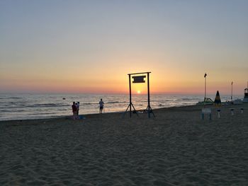 Silhouette people playing on beach against sky during sunset