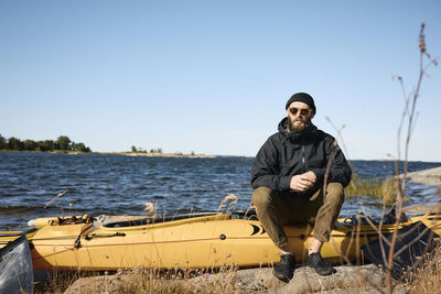 Man sitting on kayak on coast and looking at camera