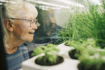Smiling senior woman looking at plants through glass