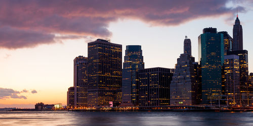 Sea by buildings against sky during sunset