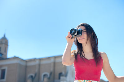 Low angle view of beautiful woman photographing by church against clear sky